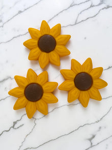 Vista zenitale di tre clicker antistress a forma di girasole con petali gialli e centro marrone, realizzati in PLA ecosostenibile.